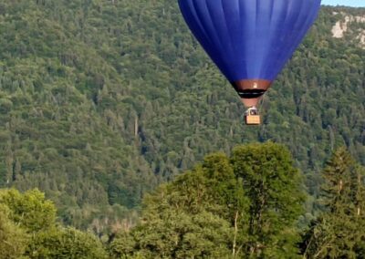 Une montgolfière bleue s'élève devant la forêt